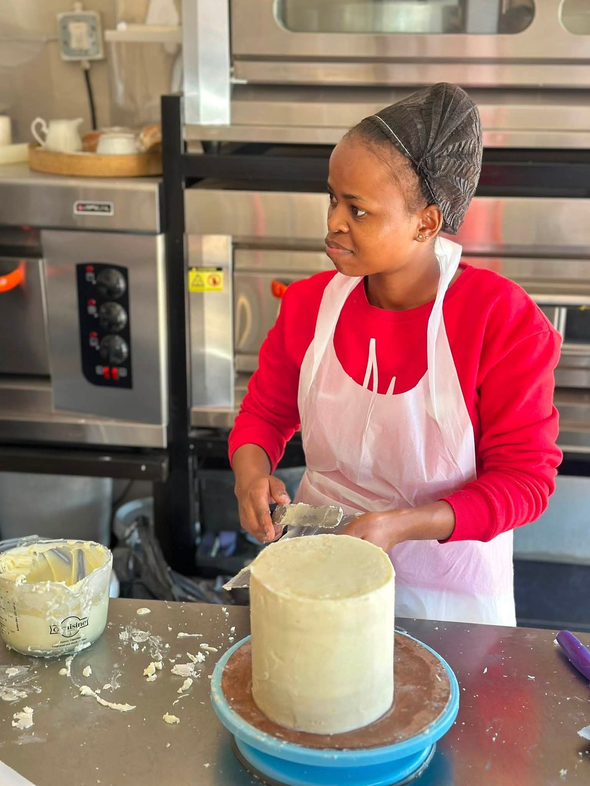 Lerato smoothing buttercream on a tall cake in a professional kitchen